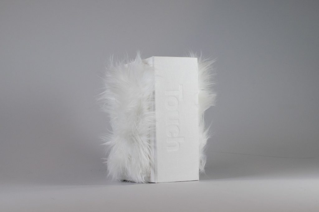 En vit låda med texten Touch på ryggen. Fram och baksidan av lådan är kladd med vit päls.
